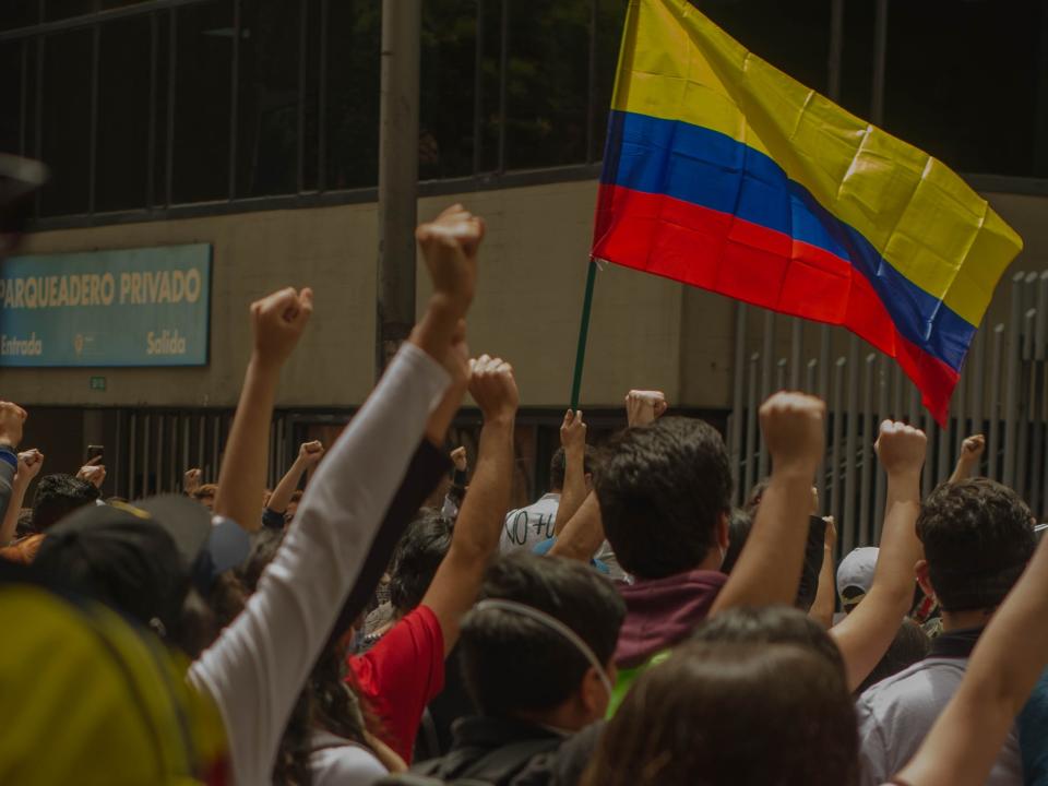Protesters raise their hands with fists. Someone is holding a Colombian flag.