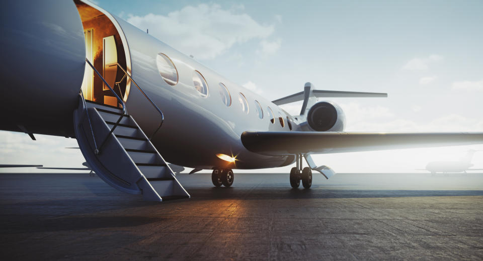 A private jet is parked on an airstrip with its door open, and a stairway is leading up to its entrance. The scene is clear and calm