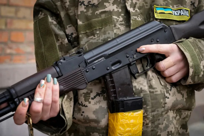 An armed civil defense woman holds a Kalashnikov assault rifle while patrolling an empty street due to a curfew in Kyiv, Ukraine, Sunday, Feb. 27, 2022.