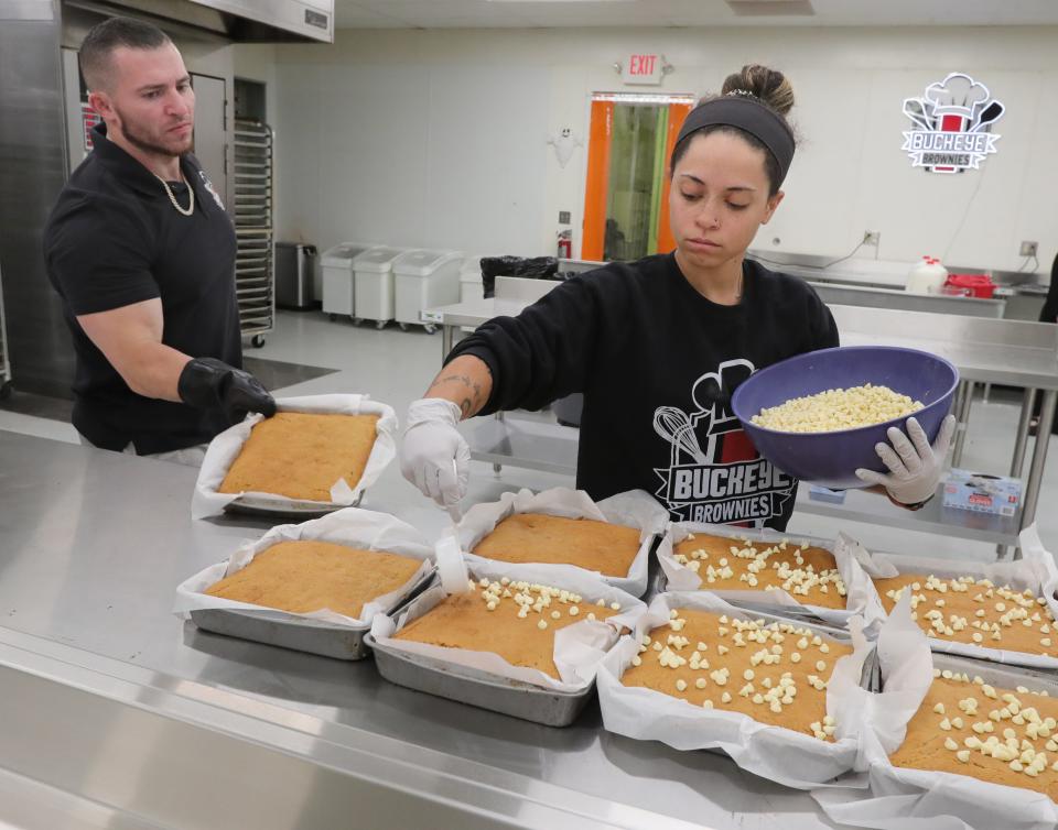 Buckeye Brownies owner Zack Buckeye removes hot pans of Butter My Biscoff brownies from a cooling rack Tuesday as Jessie McLean adds white chocolate chips on top.