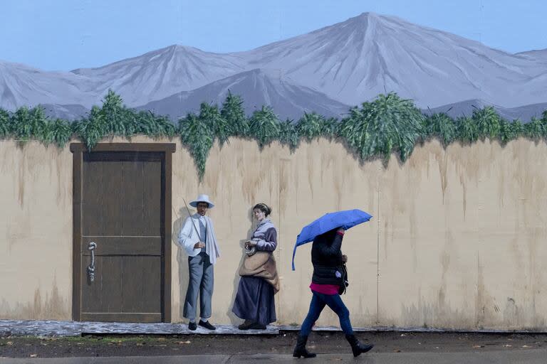 Una mujer con paraguas camina junto a un mural de la artista Elena Ho en un día lluvioso en Santiago de Chile, el jueves 13 de junio de 2024.