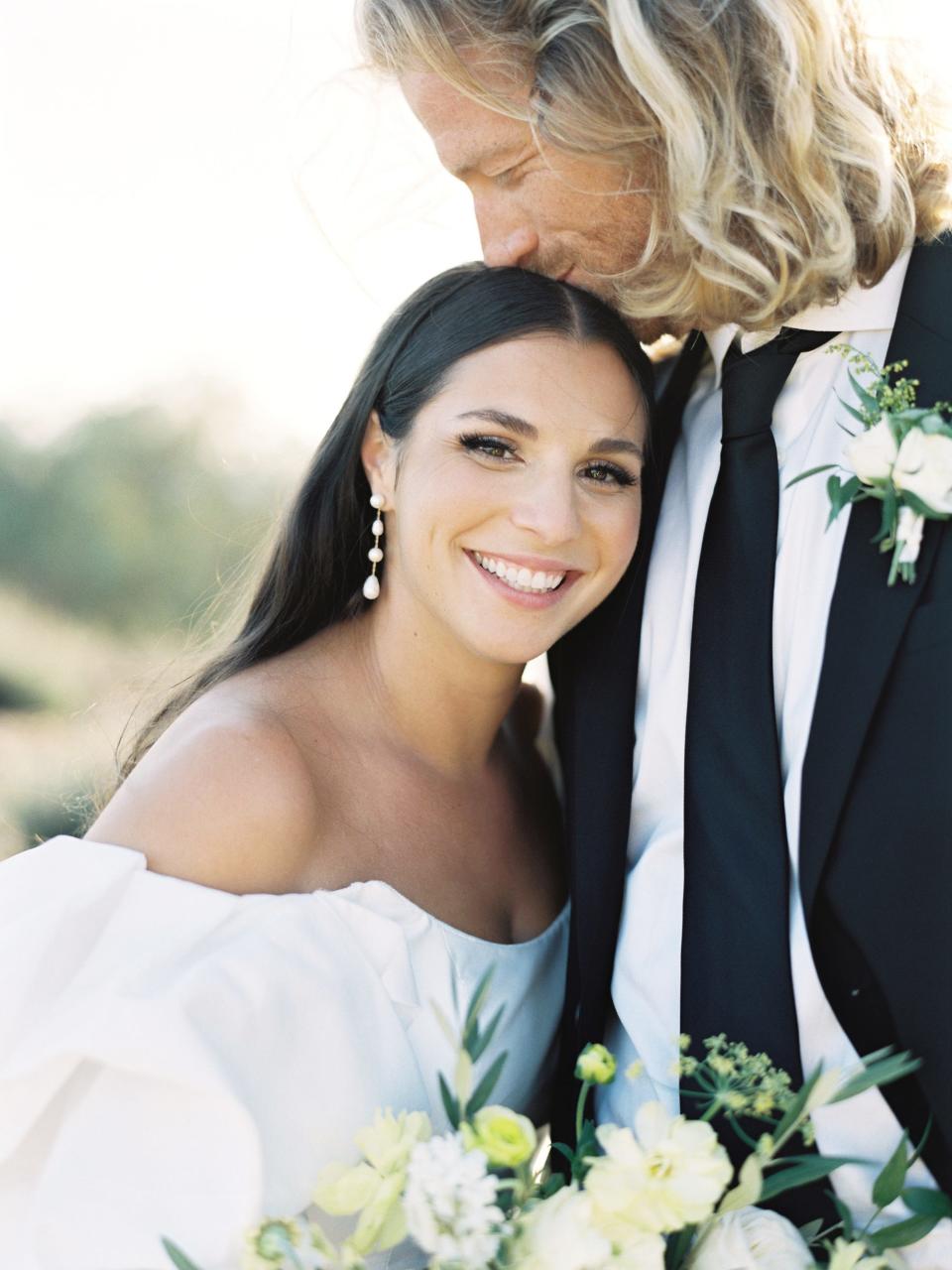 A groom kisses his bride on her head on their wedding day.