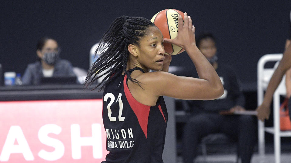 A'ja Wilson in a black Aces uniform holds the ball over her head.