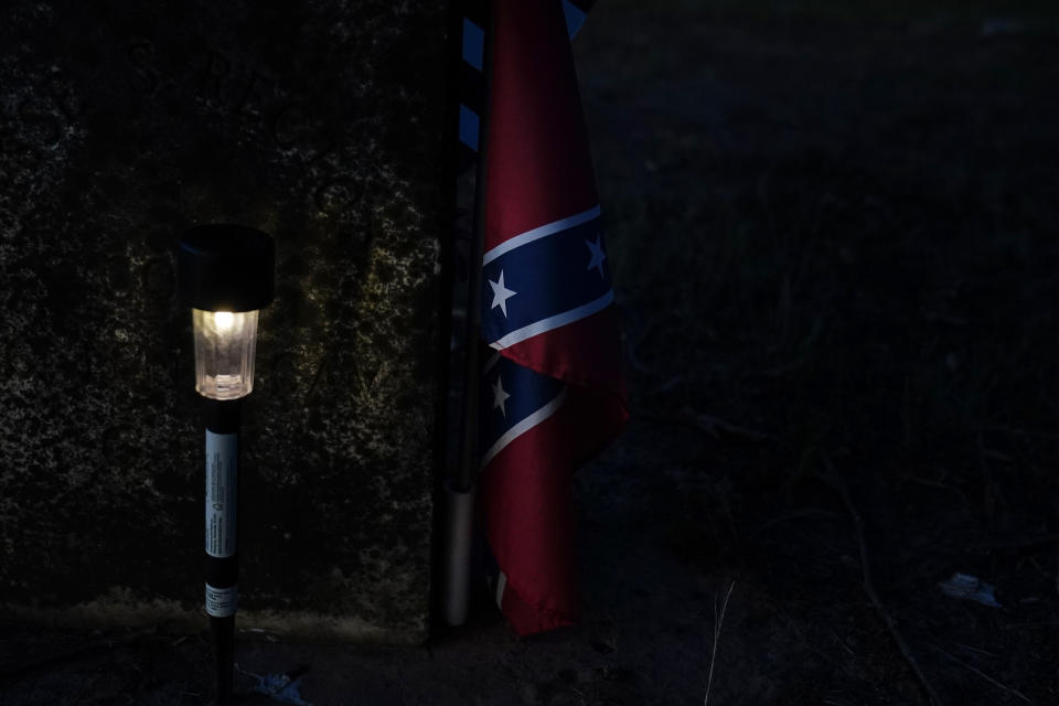 A small light illumines a confederate flag next to a grave on Thursday, June 23, 2022, in Athens, Ala., in the same cemetery David Guess was buried in March. David Guess was killed by gun violence. According to the police, Guess was shot with a handgun and burned in a wooded area with tires piled on his body and set on fire. (AP Photo/Brynn Anderson)