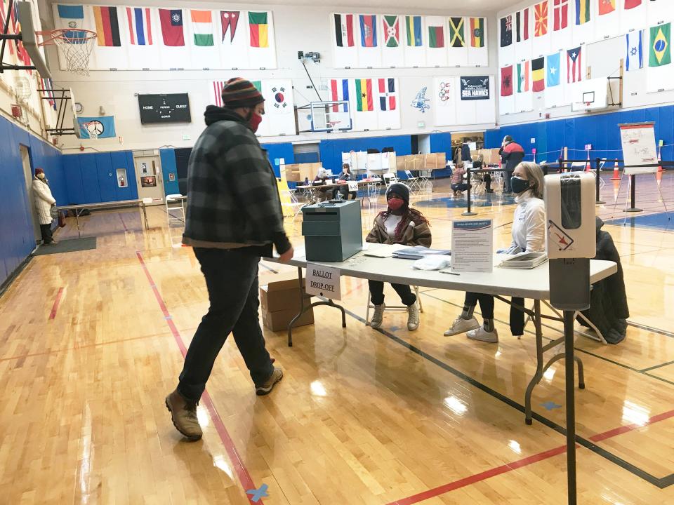 Gabriel Whitcomb-Paulson, left, prepares to deliver his drop-off ballot at Edmunds Elementary School in Burlington on March 2, 2021. He is greeted by poll workers Rehema Abdi, center, and Gloria Flinn.
