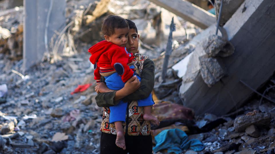 A Palestinian boy carrying a baby stands at the site of a destroyed building in Rafah, in southern Gaza, December 4, 2023. - Mohammed Salem/Reuters