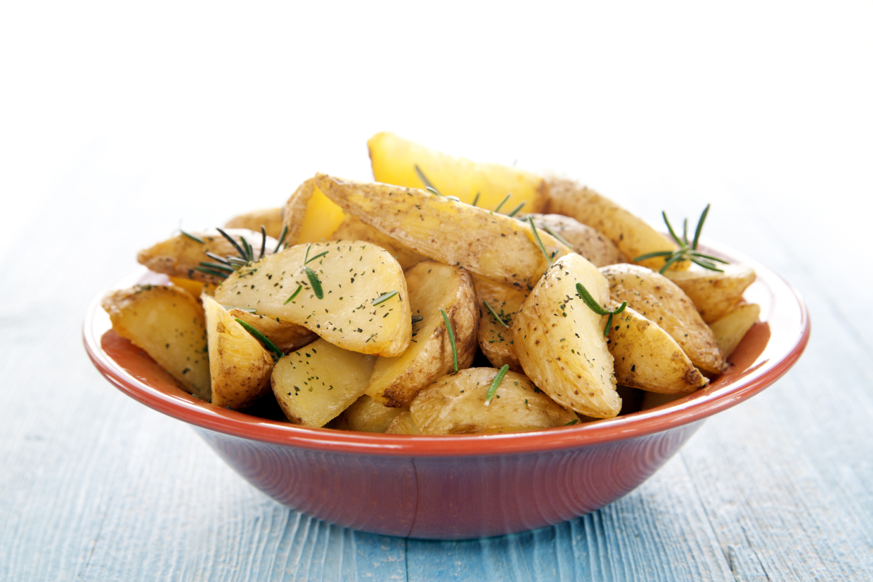 Greek lemon potatoes in a red bowl on a blue wooden table with a bright white background