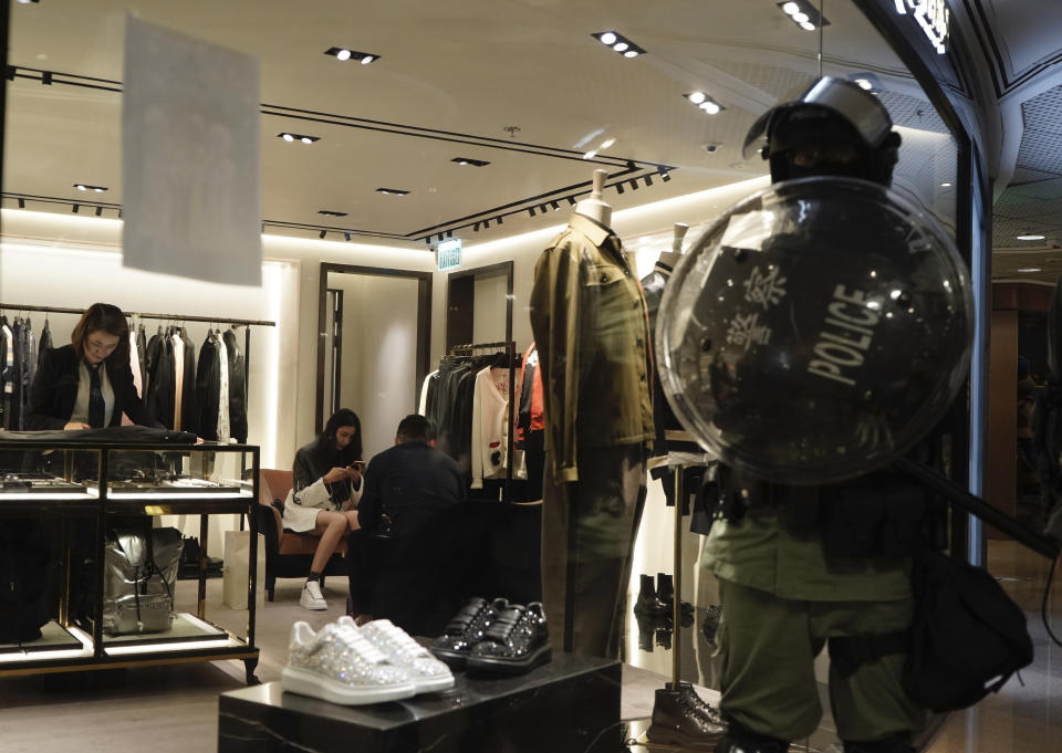 Shoppers continue to patronize retail stores as a riot police stand by in a mall on Christmas Eve in Hong Kong on Tuesday, Dec. 24, 2019. More than six months of protests have beset the city with frequent confrontations between protesters and police. (AP Photo/Kin Cheung)