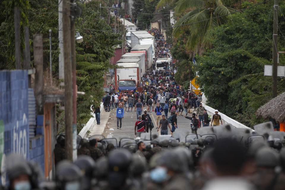 Honduran migrants, top, stand next to cargo trucks as they confront Guatemalan soldiers and police manning a roadblock the prevents them from advancing toward the US, on the highway in Vado Hondo, Guatemala, Monday, Jan. 18, 2021. The roadblock was strategically placed at a chokepoint on the two-lane highway flanked by a tall mountainside and a wall leaving the migrants with few options. (AP Photo/Sandra Sebastian)