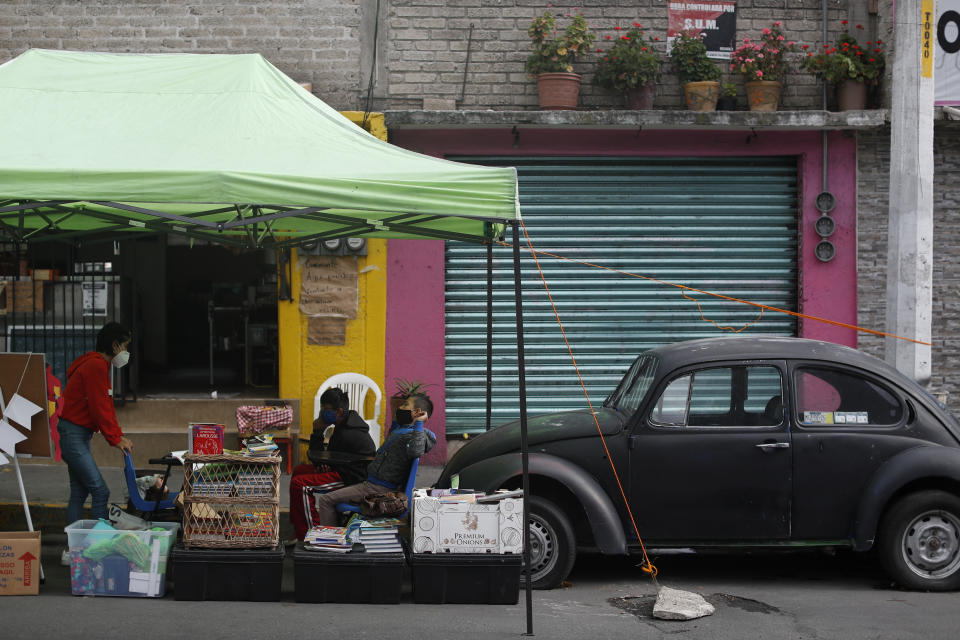 Volunteer Fatima Rodriguez, left, gives a history lesson to siblings Bryan, right, and Emanuel Quintana, in front of "Tortillerias La Abuela," or Grandma's Tortilla Shop, on the southern edge of Mexico City, Friday, Sept. 4, 2020. Concerned about the educational difficulties facing children during the coronavirus pandemic, the couple who runs the tortilla shop adapted several spaces outside their locale to provide instruction and digital access to locale children who don't have internet or TV service at home, a project which has attracted donations and a waiting list of students. (AP Photo/Rebecca Blackwell)