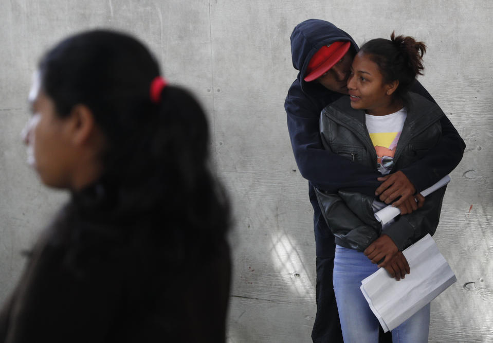 In this Dec. 4, 2018 photo, a couple embraces as they wait in line at a job fair where migrants are able to apply for Mexican work permits, recover lost Honduran identity documents and meet with potential employers in Tijuana, Mexico. Once they got their Mexican identification numbers they can meet with recruiters for assembly plants in the area where turnover is often high and jobs are always available. (AP Photo/Rebecca Blackwell)