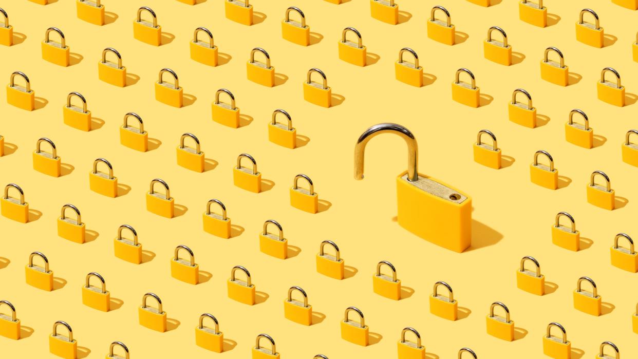  High angle view of many yellow padlocks on yellow background with one of them open. 