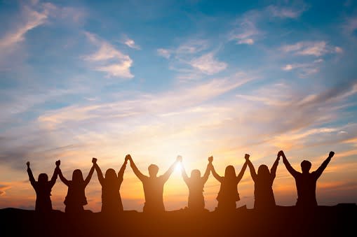 People holdings hands in front of sunset