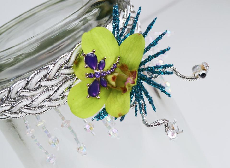 This product image released by Gillespie Florists, Inc. shows a floral headband made with a green orchid, dragonfly pin, dangling beads, blue glittered leaves, silver accent ribbon, rhinestones and a braided silver and white headband. (AP Photo/Gillespie Florists, Inc.)