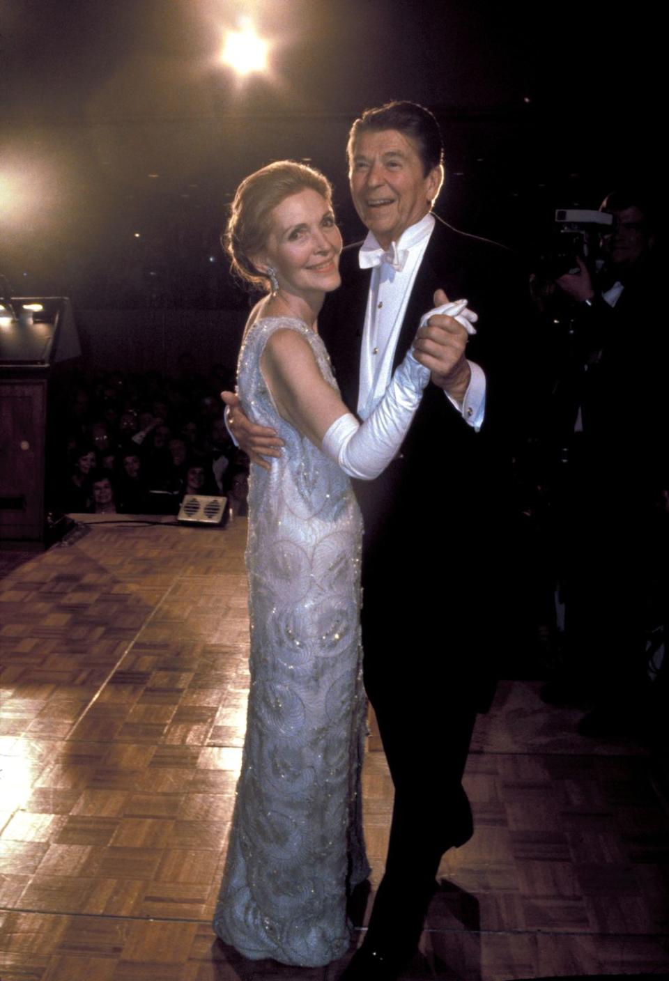 <p>President Reagan shares his first dance with his wife, Nancy Reagan. No stranger to a black tie event, the former Hollywood actress stunned in a white one-shoulder column gown with silver beading, designed by James Galanos.</p>