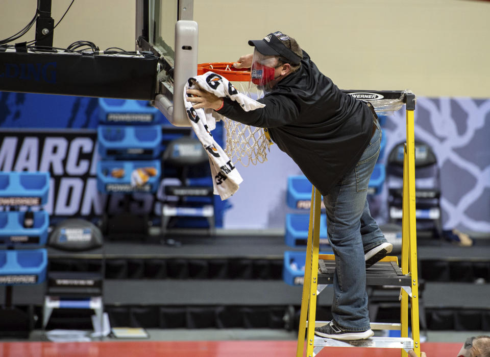 A worker cleans the backboard and rim on the court during halftime of a First Four game between Texas Southern and Mount St. Mary's in the NCAA men's college basketball tournament Thursday, March 18, 2021, in Bloomington, Ind. (AP Photo/Doug McSchooler)