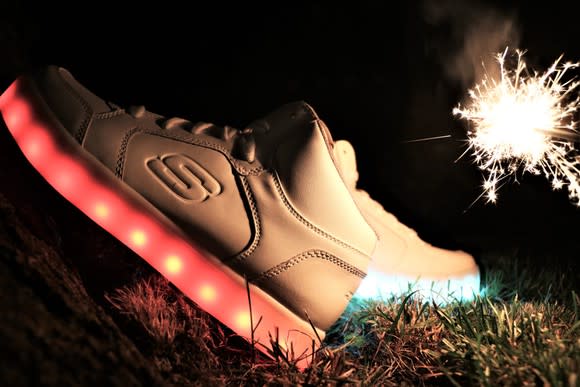 A pair of Skechers shoes in the dark with lighted soles and a sparkler lighting the background.