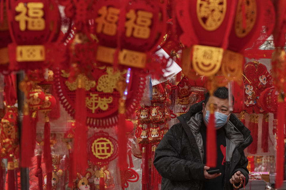 A man wearing a face mask shops for Chinese Lunar New Year decorations at a pavement store in Beijing, Saturday, Jan. 7, 2023. China has suspended or closed the social media accounts of more than 1,000 critics of the government's policies on the COVID-19 outbreak, as the country moves to further open up. (AP Photo/Andy Wong)