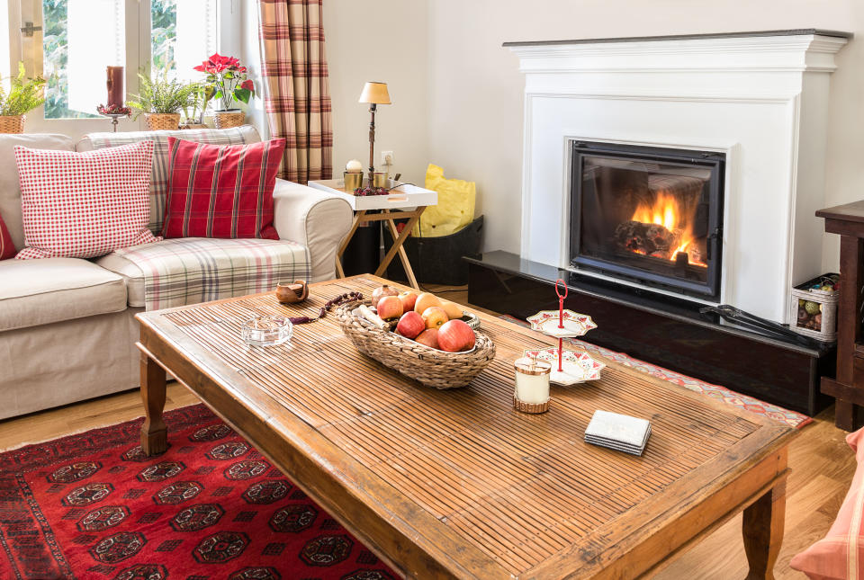 Interior living room with fireplace, two seater sofa, red carpet, a wooden coffee table on an oak floor.