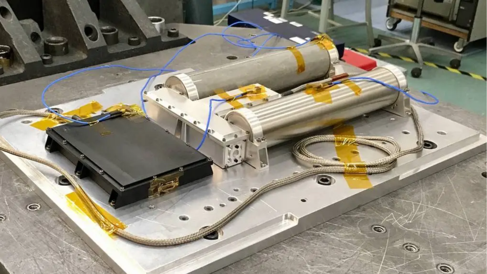 a piece of scientific equipment, with wires and cables, sits on a silver metallic lab bench.