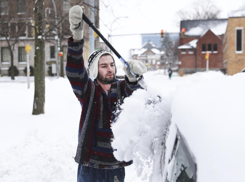 Kyle Teed scrapes snow off of his friend's car in Buffalo, N.Y.'s Elmwood Village on Monday, Dec. 26, 2022. Clean up is currently under way after a blizzard hit four Western New York counties. (Joseph Cook/The Buffalo News via AP)