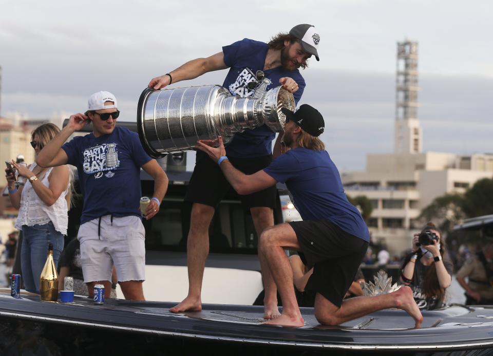Tampa Bay Lightning' Victor Hedman pours a drink from the Stanley Cup into the mouth of Steven Stamkos during the NHL hockey Stanley Cup champions' boat parade, Wednesday, Sept. 30, 2020, in Tampa, Fla. At left is Luke Shenn. (Dirk Shadd/Tampa Bay Times via AP)