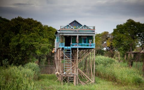 A woman sweeps the porch of her colourful stilt house - Credit: GETTY