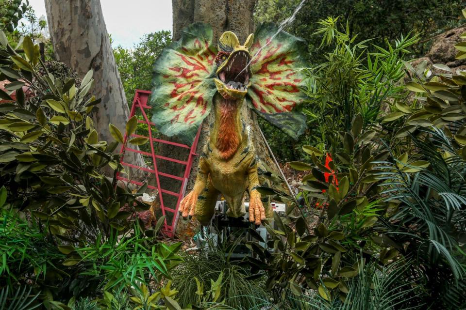 A dinosaur breaks tout of a cage in a jungle.