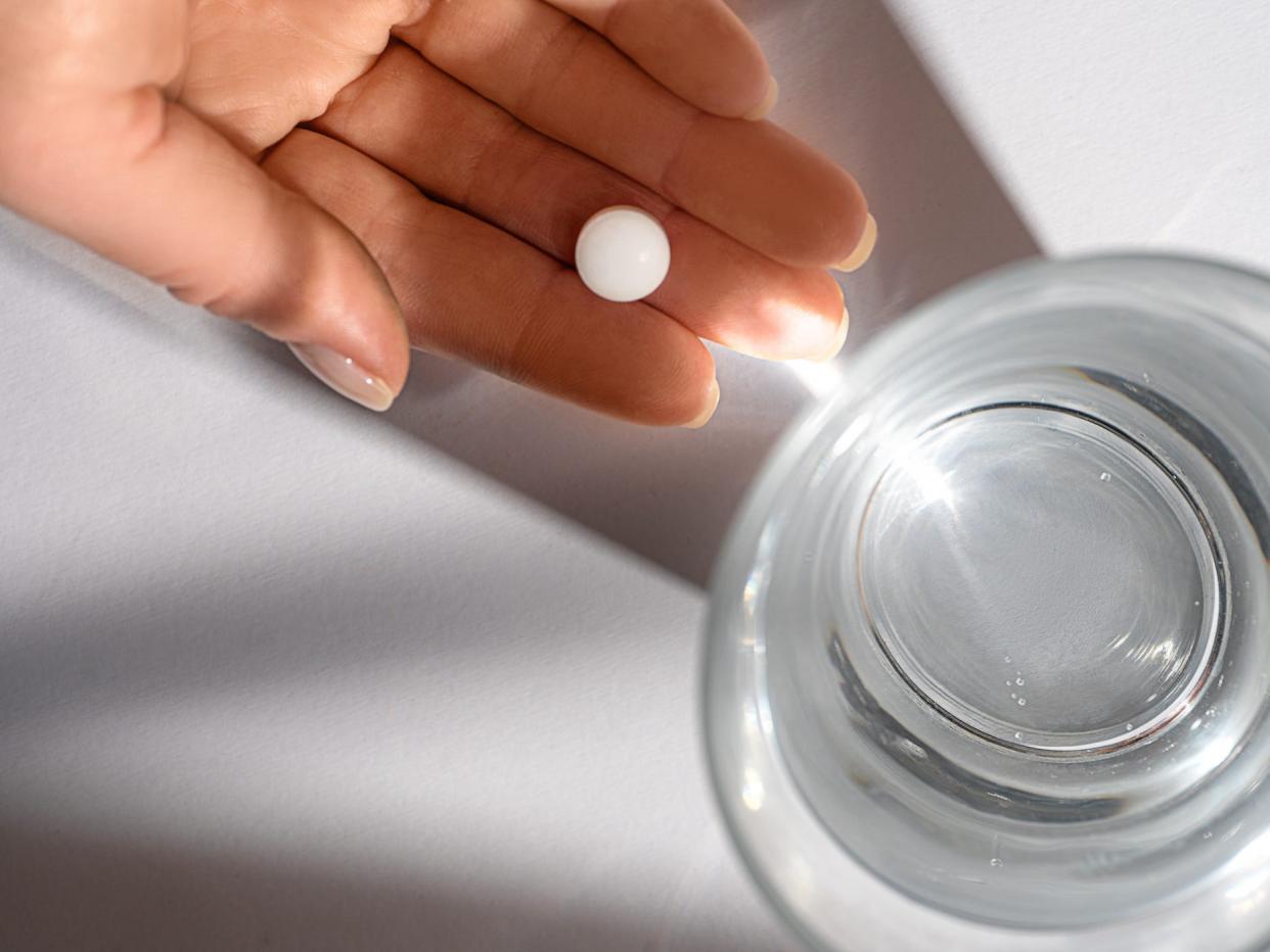 a pill in someone's hand, next to a glass of water