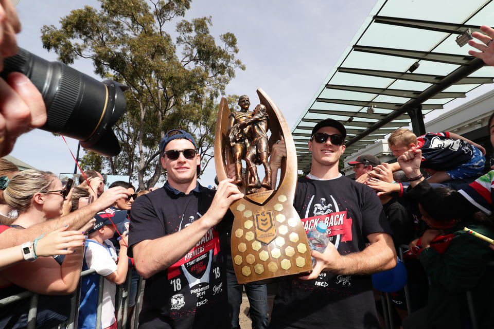 Luke Keary and Sam Verrills hold up the NRL premiership trophy in front of a crowd.