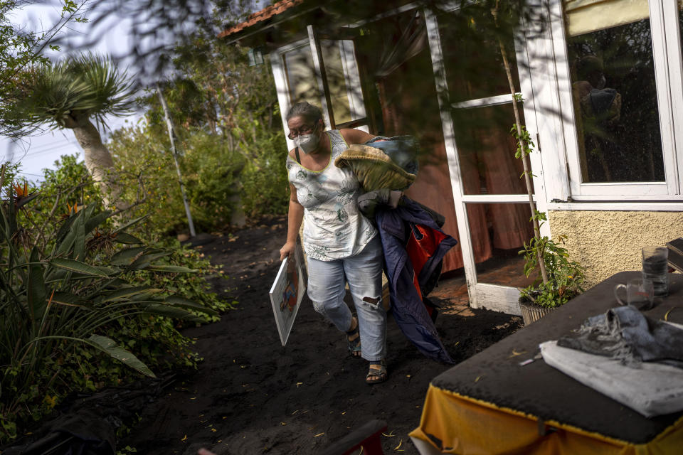 Annette Lowestein, from Germany, collects some of her belongings while leaving her house stalked by the lava that advances towards her neighborhood on the Canary island of La Palma, Spain, Saturday, Oct. 30, 2021. An erupting volcano in the Spanish island of La Palma continued to emit vast amounts of magma, gases and ash on Saturday, after days of intense seismic activity and more than five weeks since it erupted. (AP Photo/Emilio Morenatti)