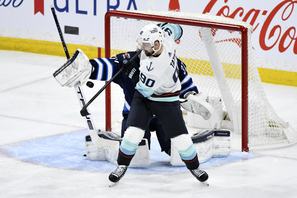 Seattle Kraken's Tomas Tatar (90) deflects a shot past Winnipeg Jets goaltender Connor Hellebuyck (37) for a goal during the third period of an NHL hockey game Tuesday, March 5, 2024, in Winnipeg, Manitoba. (Fred Greenslade/The Canadian Press via AP)