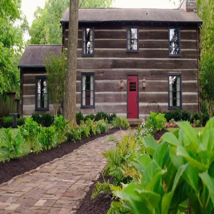 There is a brick pathway that leads to the unique red door on the front of the log cabin