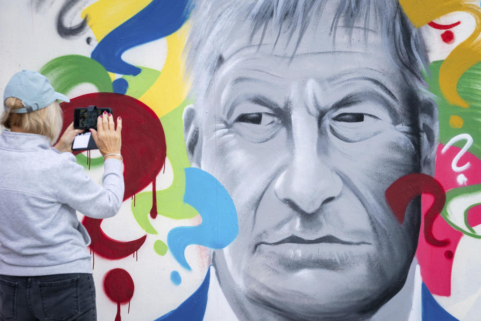 A person takes a photograph of 'Why', a mural of David Amess by local Artist Madmanity, at a skate park in Leigh-on-Sea, Essex, England, Monday, Oct. 18, 2021. British Prime Minister Boris Johnson will lead tributes in Parliament to David Amess, a Conservative lawmaker stabbed to death as he met constituents. The attack shocked Britain, and it has fueled concern about politicians’ safety and the level of vitriol directed at them. It came five years after Labour Party lawmaker Jo Cox was murdered by a far-right extremist. (Aaron Chown/PA via AP)