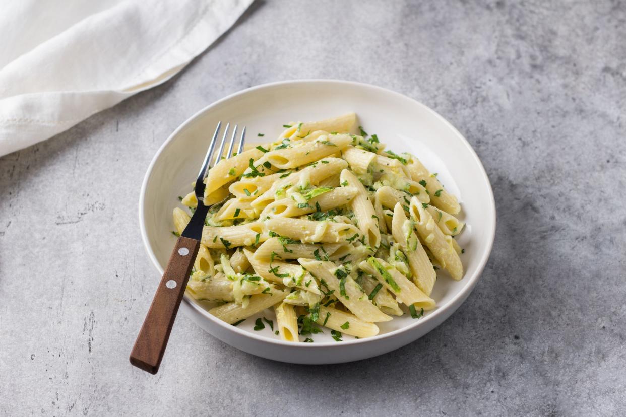 Penne pasta with zucchini, cream cheese and herbs on a gray textured background, top view. Vegetarian food, homemade healthy food.