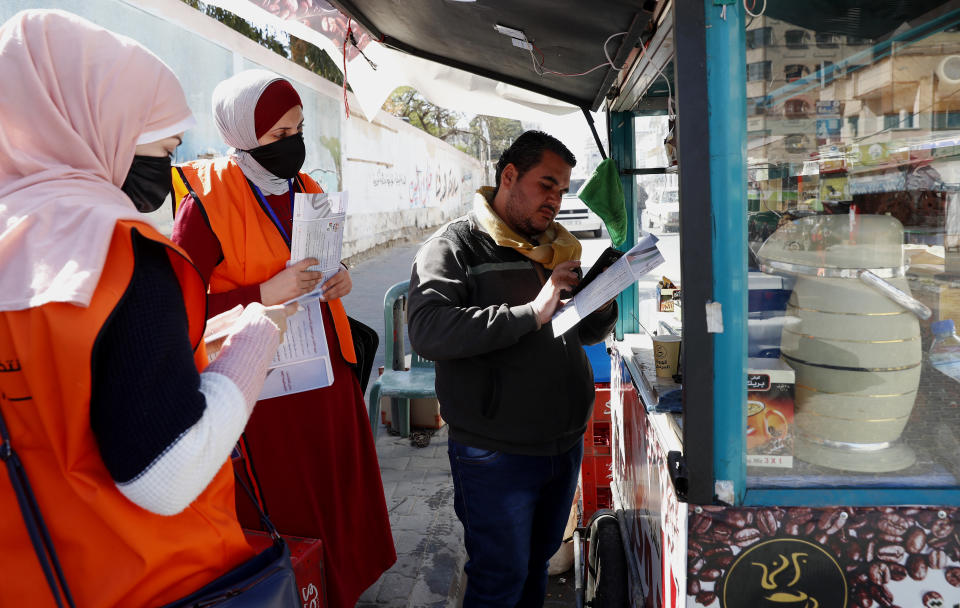 Members of Central Elections Commission's filed teams register Mohammed Al-Jawabra, right, a street coffee vendor, to the electoral roll, at the main road of Gaza City, Feb. 10, 2021. Palestinian poll workers fanned out across the Gaza Strip on Wednesday, where they found voters eager to register ahead of elections that could serve as the first referendum on Hamas' rule since the militant group seized power more than a decade ago. (AP Photo/Adel Hana)