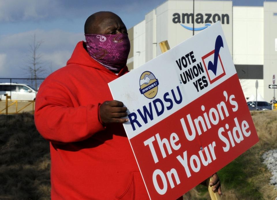 FILE - In this Tuesday, Feb. 9, 2021, file photo, Michael Foster of the Retail, Wholesale and Department Store Union holds a sign outside an Amazon facility where labor is trying to organize workers in Bessemer, Ala. When Amazon found out that workers were trying to form a union, a worker said Wednesday, March 17, that the company put up signs across the warehouse in Bessemer, Ala., including in bathroom stalls. (AP Photo/Jay Reeves, File)