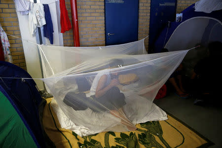 A migrant sits under a mosquito net inside the disused Hellenikon airport, where refugees and migrants are temporarily housed, in Athens, Greece, July 13, 2016. REUTERS/Alkis Konstantinidis/File Photo