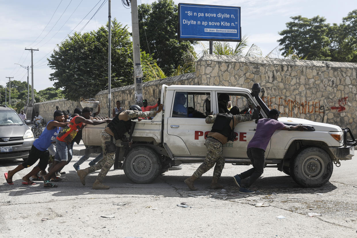 FILE - People push a police car that ran out of gas, in Port-au-Prince, Haiti, Oct. 27, 2021. The U.S. government is urging U.S. citizens to leave Haiti given the country’s deepening insecurity and a severe lack of fuel that has affected hospitals, schools and banks. Gas stations remained closed on Thursday, Nov. 11, 2021, a day after the State Department issued its warning. (AP Photo/Odelyn Joseph, File)