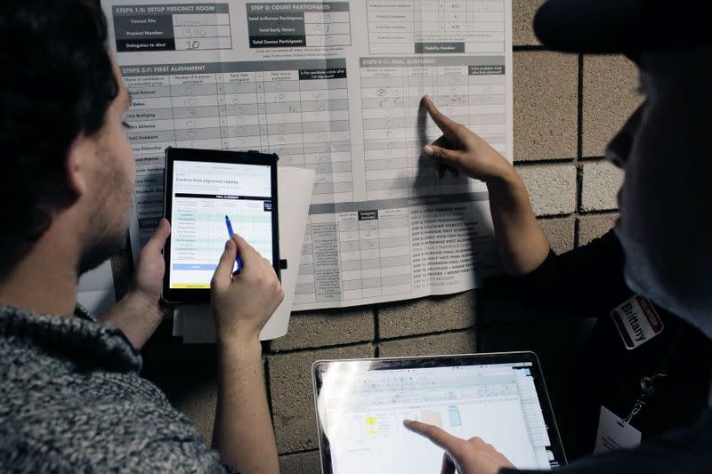 Volunteers use an iPad while a voter double checks caucus results using a spreadsheet on his laptop at a Nevada Caucus voting site at Coronado high school in Henderson