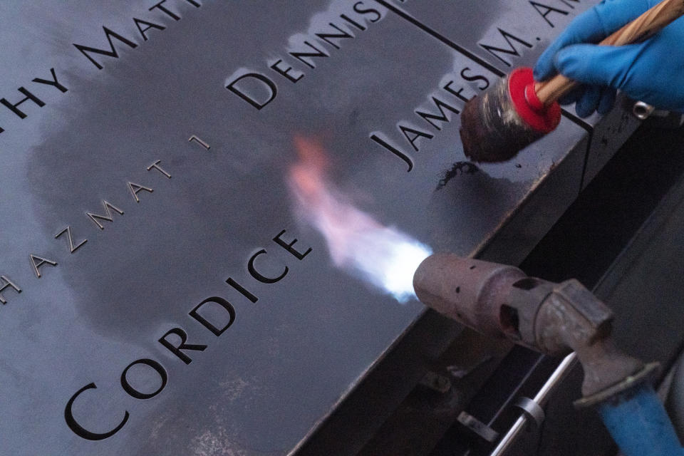 Kevin Hansen, an engineer at the September 11 Memorial, uses a torch to clean and burnish the names cut into the metal plates that border the south pool, Wednesday, Aug. 4, 2021, in New York. During a pause from his work, Hansen says, "We do it for their memorial. They have to be remembered. We do it for the family members, the people that are suffering still from that day, and of course all the people that we lost that day." (AP Photo/Mark Lennihan)