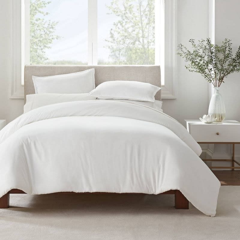 A neatly made bed with white bedding and pillows, in a bright room for an article on shopping for home essentials