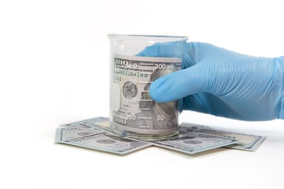 Gloved hand holding a beaker with cash inside.