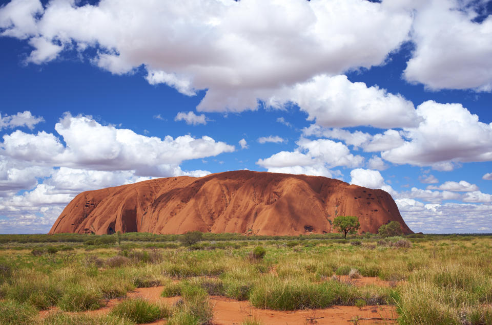 Uluru, Northern Territory, Australia - March 29, 2016: Fluffy clouds drift over Uluru (also known as Ayers Rock) in the Australian Outback. A genuine Wonder of the Natural World (and a UNESCO World Heritage Site), it's also a sacred place to the local Anangu people.