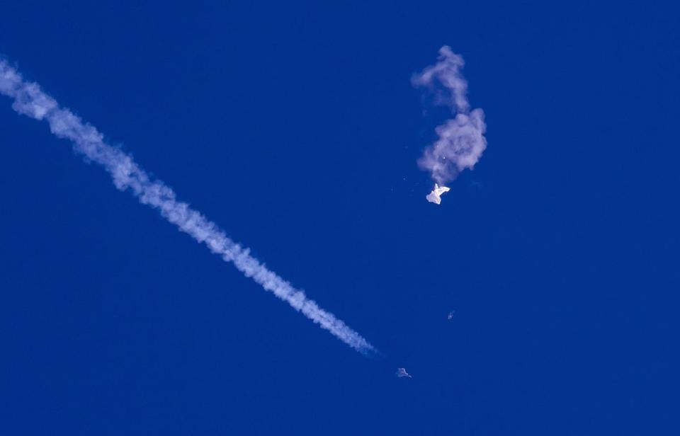 In this photo provided by Chad Fish, the remnants of a large balloon drift above the Atlantic Ocean, just off the coast of South Carolina, with a fighter jet and its contrail seen below it on 4 February (AP)
