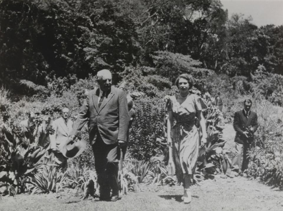 A man and a woman are seen walking next to a lush garden.