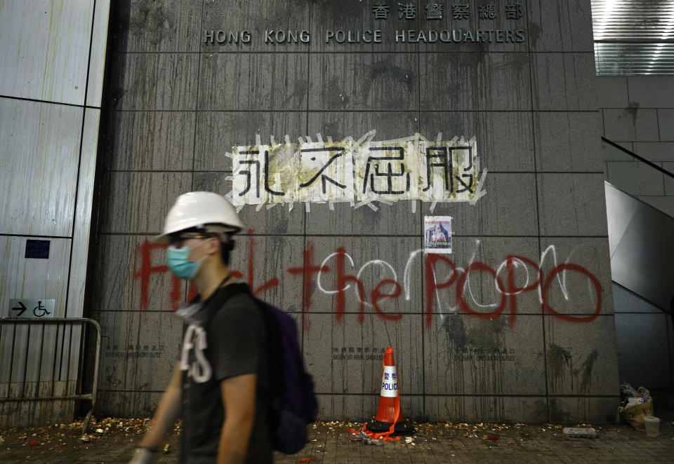 A protester walks past a wall outside the police headquarters with eggs thrown by protestors and a banner reading "Never Give In" in Hong Kong, Friday, June 21, 2019. More than 1,000 protesters blocked Hong Kong police headquarters into the evening Friday, while others took over major streets as the tumult over the city's future showed no signs of abating. (AP Photo/Vincent Yu)