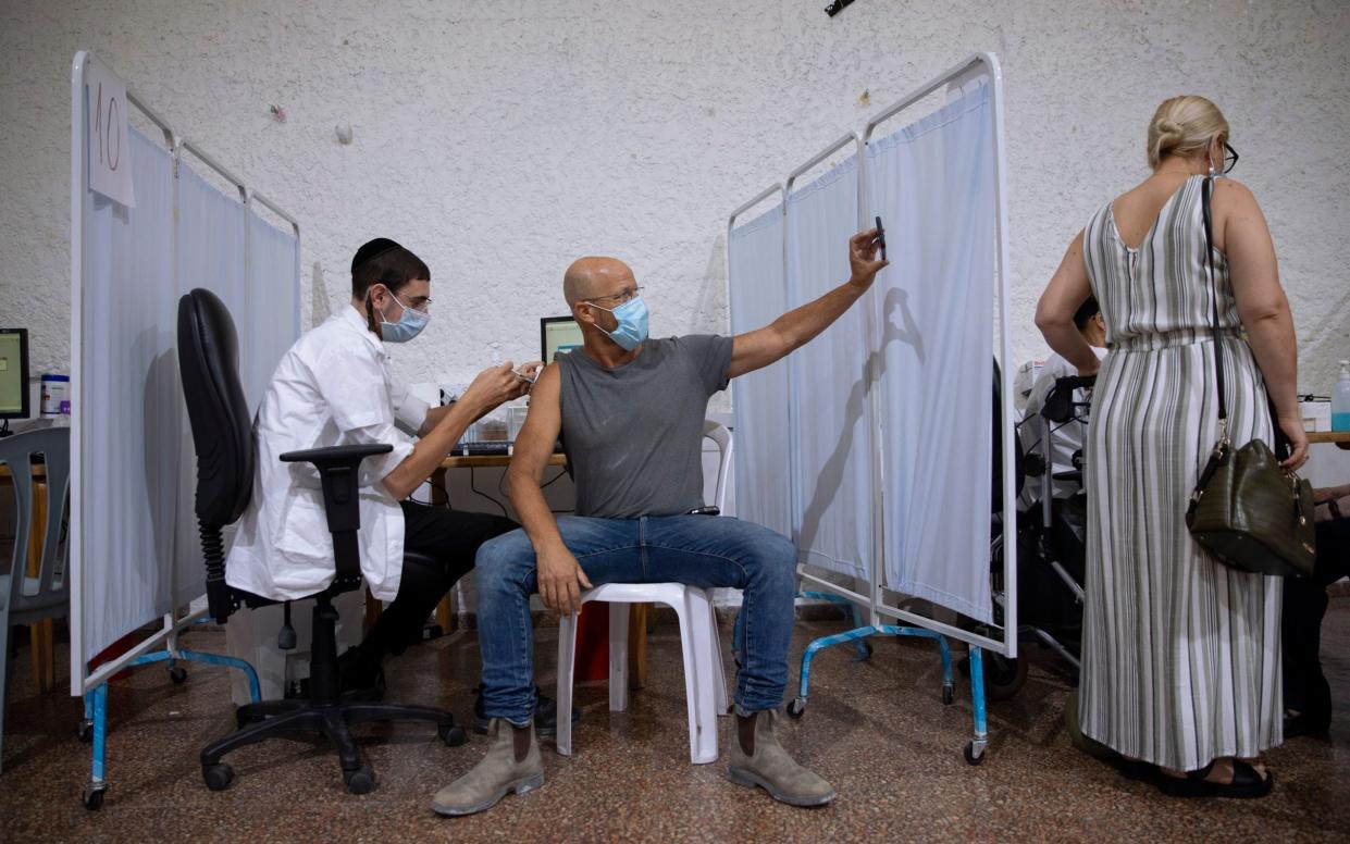 An Israeli man takes a selfie while receiving his third Pfizer vaccine - Oded Bality