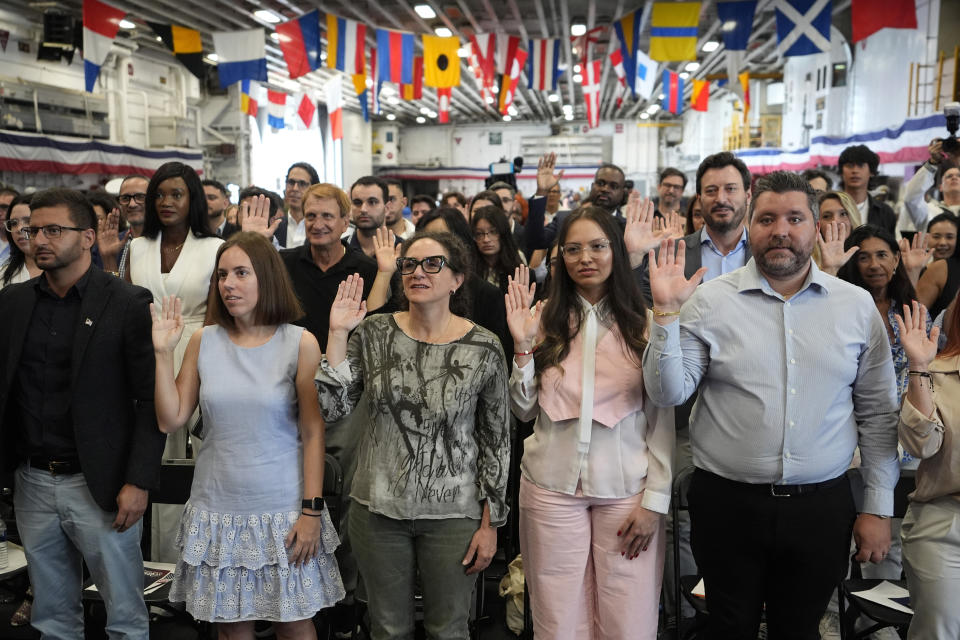 People raise their right hand as they take the Oath of Allegiance to the United States of America during a naturalization ceremony aboard the USS Bataan during Fleet Week Miami at PortMiami, Tuesday, May 7, 2024, in Miami. (AP Photo/Lynne Sladky)