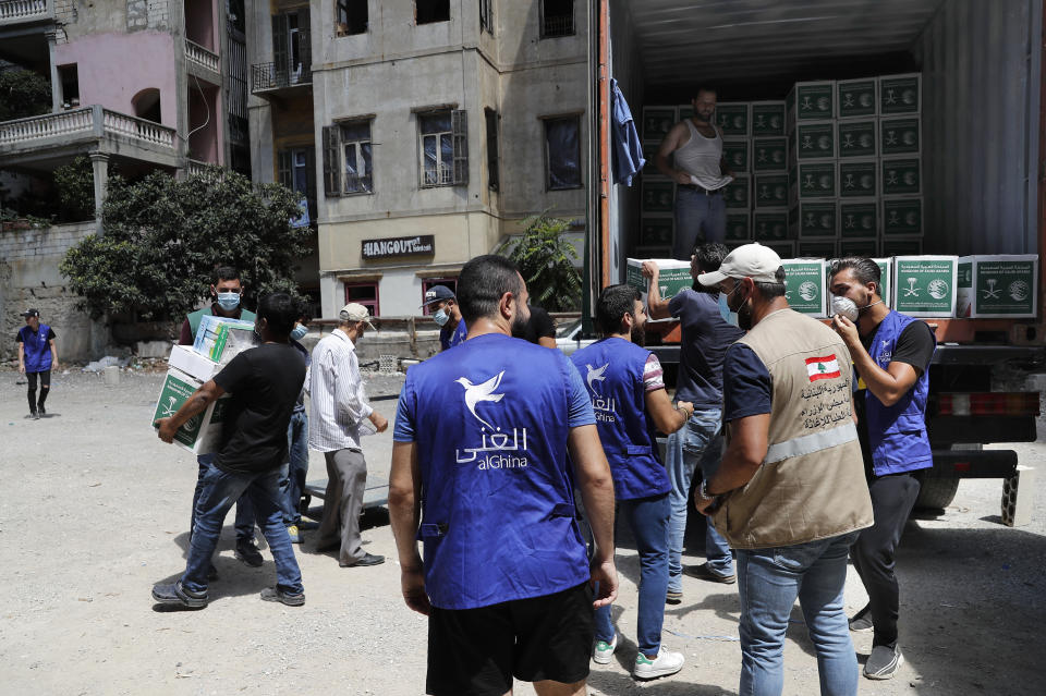 Members of the al-Ghina NGO distribute boxes of food for people in need, near the scene of last week's explosion, in Beirut, Lebanon, Tuesday, Aug. 11, 2020. In the absence of the state, acts of kindness and solidarity have been numerous and striking. Many extended a helping hand far beyond their circle of friends or family, taking to social media to spread the word that they have a room to host people free of charge. And on the streets, it was young volunteers with brooms, not government workers, who swept the streets littered with shattered glass. (AP Photo/Hussein Malla)